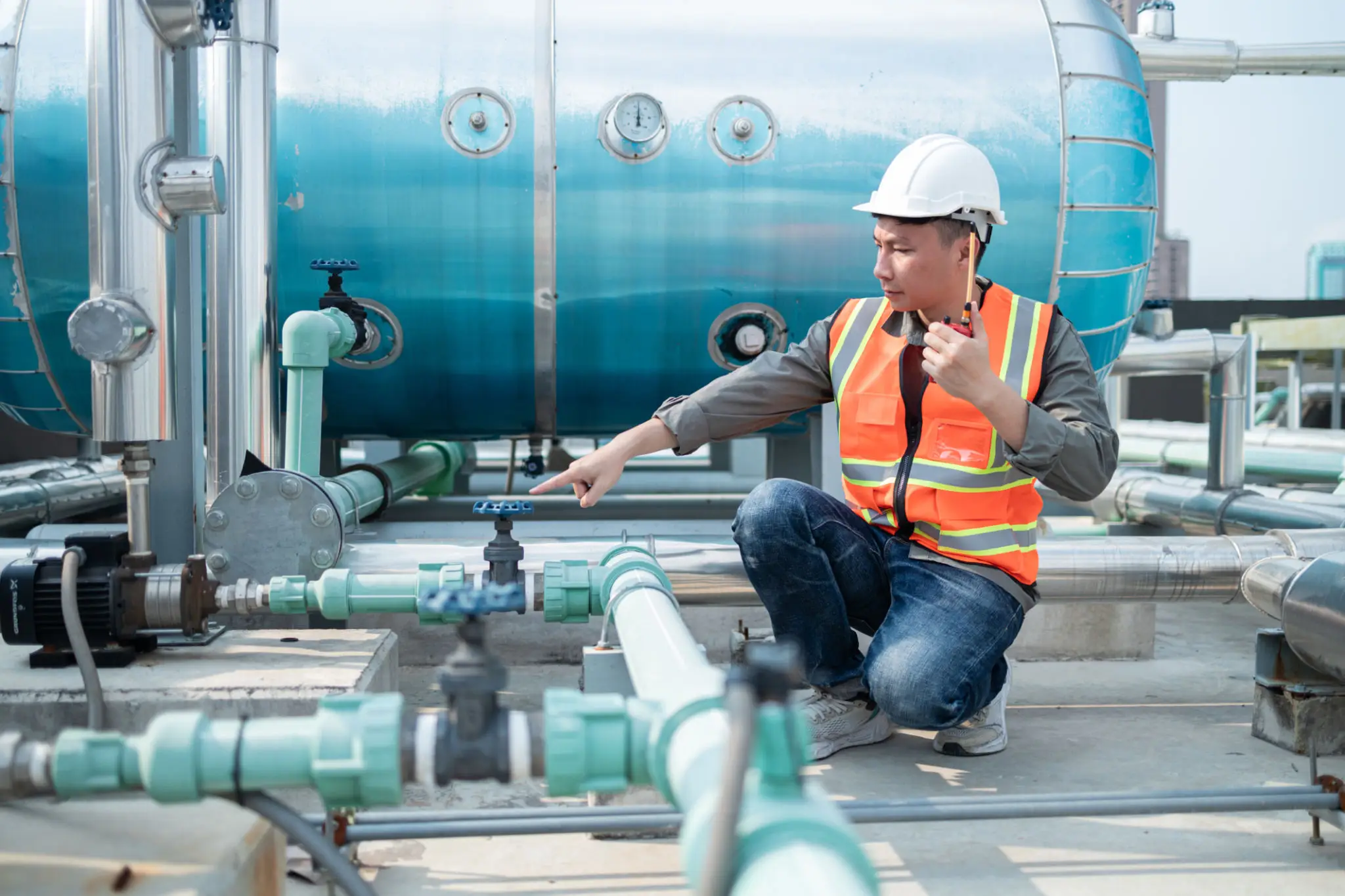 Worker inspecting industrial pipes, wearing safety gear.